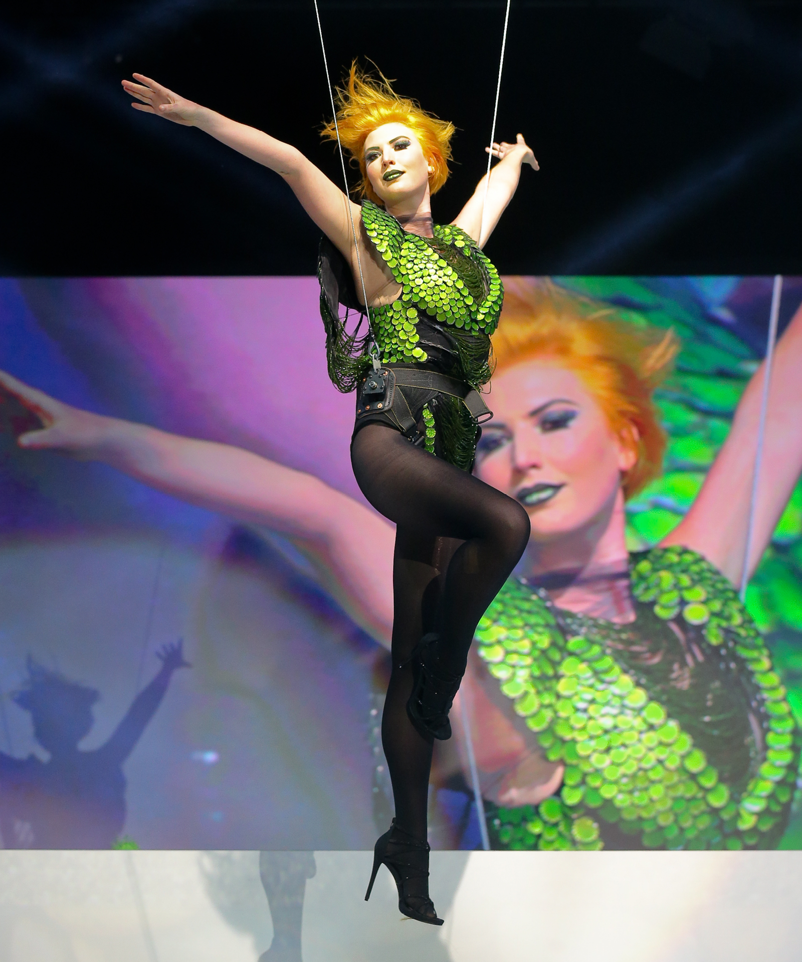 Redhaired Girl in green dress attached to strings flying at Paul Mitchell Event